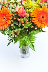 Detail of a bouquet of orange, yellow and red flowers in a vase on a white background with space for copy text.