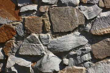 Wall background paved with stones of different irregular shapes on cement mortar.