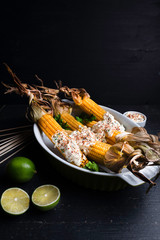 Baked corn cobs in a spicy sauce with lime on a dark background