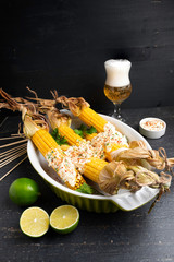 Baked corn cobs in a spicy sauce with lime on a dark background