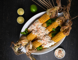 Baked corn cobs in a spicy sauce with lime on a dark background