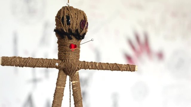 Voodoo doll with needles turns round slowly on white background with creepy symbols. Dark magic concept