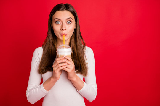 Photo of surprised girl astonished with taste of coffee she is sucking with straw while isolated with red background