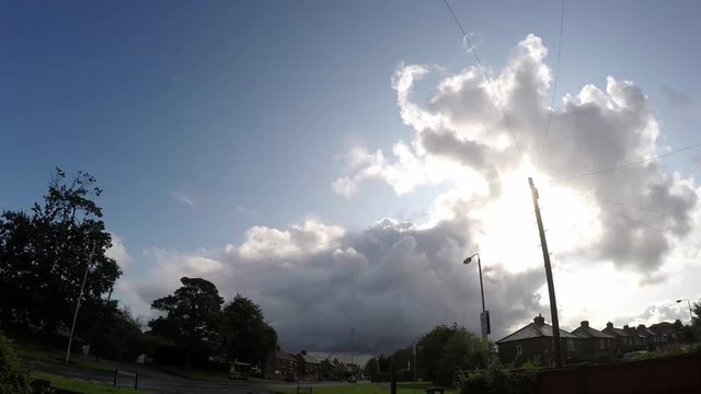 Clouds time lapse imploding above British urban town scene. Fast moving traffic on road below.