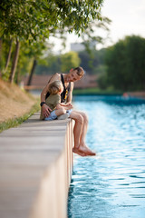 Image of young man and boy sitting on wooden bank by river