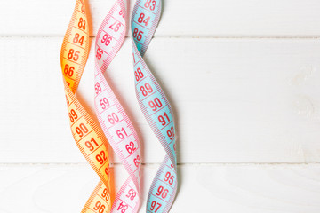 Top view of spiral colorful measure tapes on wooden background. Concept of perfect female figure...