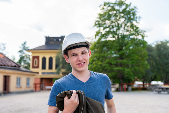 Outdoor front view portrait of a smiling young man wearing a white hard hat. Preparation for underground exploration.