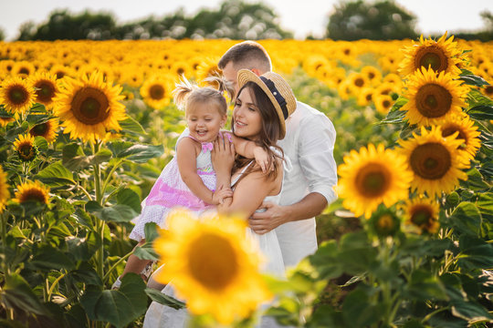 Happy family on a walk among field of sunflower. Little daughter in the arms of mother.