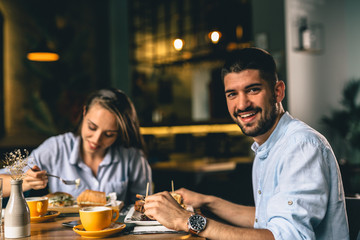 portrait of a man smiling while eating in restaurant with his girlfriend