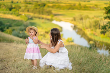 Fototapeta premium Cute little girl in a big straw hat looking at camera. Her mother near . Summer meadow at background