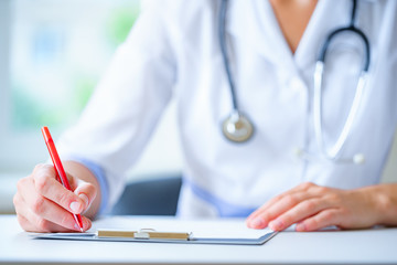 A doctor with a stethoscope writing diagnosis and therapy of the disease in a clipboard during a...