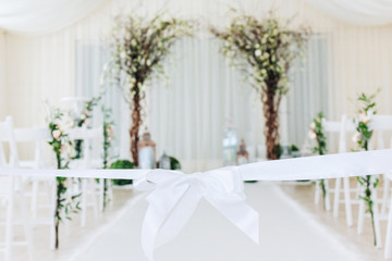 Indoor wedding ceremony with white wedding arch decorated with flowers and big white candles