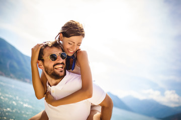 Handsome young man giving piggyback ride to girlfriend on beach. Romantic young couple enjoying...