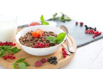 Cereal chocolate balls in bowl with milk on rustic wooden table Healthy tasty breakfast chocolate balls with strawberries, raspberries, black currants and red currants.