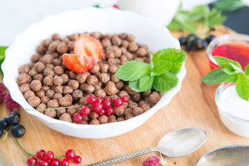 Cereal chocolate balls in bowl with milk on rustic wooden table Healthy tasty breakfast chocolate balls with strawberries, raspberries, black currants and red currants.