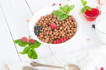 Cereal chocolate balls in bowl with milk on rustic wooden table Healthy tasty breakfast chocolate balls with strawberries, raspberries, black currants and red currants.