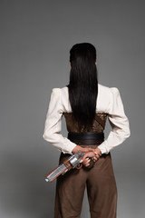 back view of steampunk woman holding vintage pistol on grey