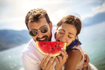 Young smiling couple eating watermelon on the beach having fun.