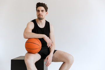 Concentrated serious strong young sports man basketball player holding ball isolated over white background.