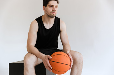 Concentrated serious strong young sports man basketball player holding ball isolated over white background.