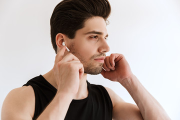 Handsome concentrated young sports man isolated over white wall background listening music with earphones.