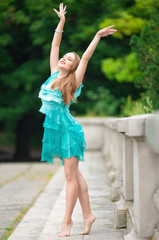 Beautiful shapely woman in a turquoise dress dancing in the park