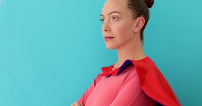 Beautiful lady dressed in superhero cape confidently looking at camera and smiling against blue background