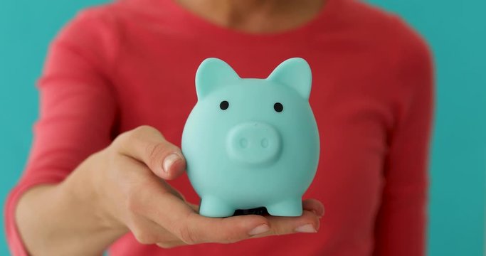 Crop prudent female in bright pink dress putting savings in piggy bank against blue background