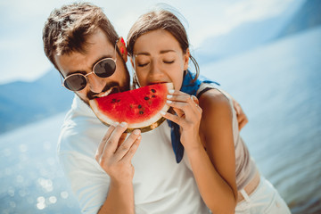 Young smiling couple eating watermelon on the beach having fun.