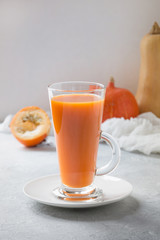 Pumpkin juice in glass on grey. Autumn, fall or winter hot drink. Cozy healthy beverage.