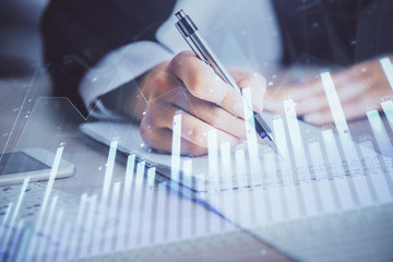 A woman hands writing information about stock market in notepad. Forex chart holograms in front. Concept of research. Multi exposure
