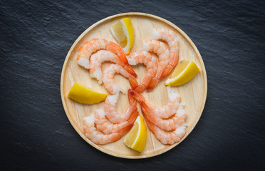 fresh shrimps served on wooden plate - boiled peeled shrimp prawns cooked with spices lemon on dark background in the seafood restaurant , top view