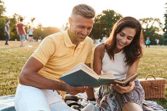 Portrait of happy middle-aged couple man and woman smiling and reading books in summer park