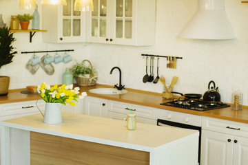 Picture of bright kitchen at daylight with big white table and yellow flowers on it 