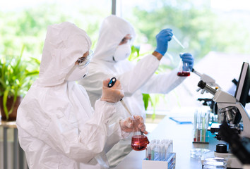 Scientists in protection suits and masks working in research lab using laboratory equipment:...