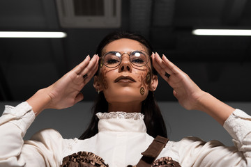 low angle view of steampunk woman touching glasses and looking at camera