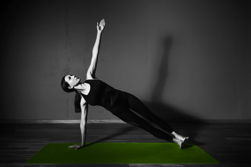 Black white photo of Young beautiful woman brunette in black clothes practice yoga kumbhakasana in dark studio green mat Sport meditation monochrome