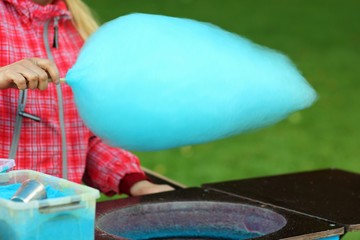 Closeup of salesman rolling bright blue cotton candy in the floss machine. People at work concept