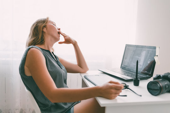 A young woman yawns in the workplace. Fatigue and overload in office work