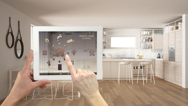 Smart remote home control system on a digital tablet. Device with app icons. Minimalist modern bright kitchen in the background, architecture interior design