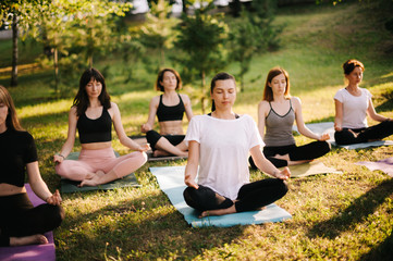 Group of mixed age women is practicing yoga and meditating morning in city park while sunrise....