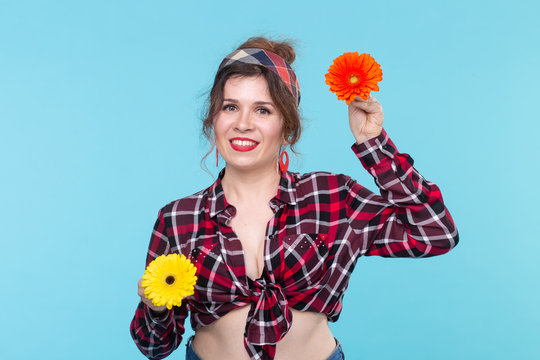 Charming young smiling woman holding two red and orange flower in her hands posing on a blue background. Concept of beauty and self-care.