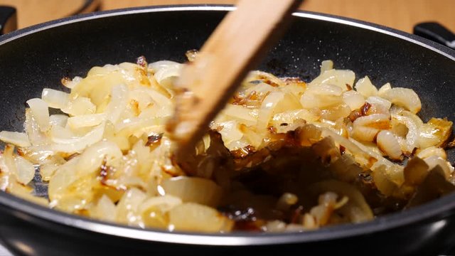Chopped onions fried  in hot frying pan, hand mixing with wooden spoon spatula. Vegetable preparing, meals with vegetables. Slow motion