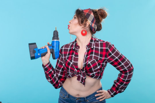 Nice young woman in retro clothes holding a in her hands depicting a pistol on a blue background. Concept of repair and construction