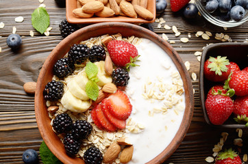 Flat lay top view at Fruit healthy muesli with banana strawberry almonds and blackberry with yogurt  in clay dish on wooden kitchen table
