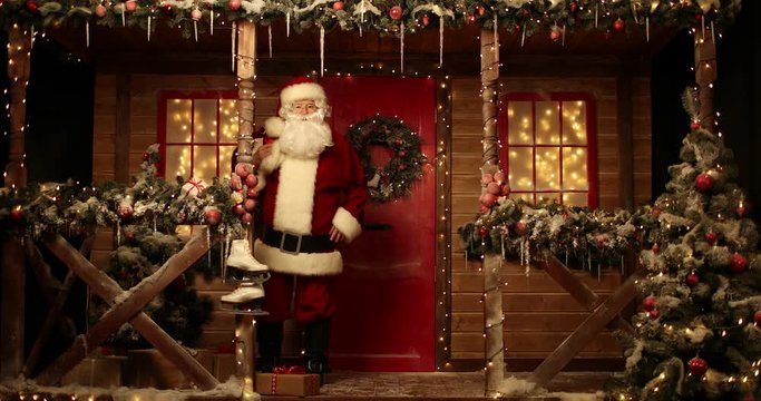 Santa Claus walks with a bag of gifts on the porch, knocks on the window and laughs on the porch of the house decorated for Christmas.