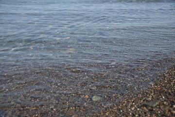 sea pebble beach with stones, transparent waves with foam, on a warm summer day