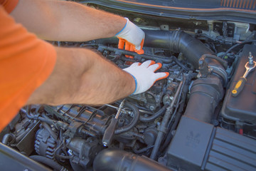 The mechanic is repairing the car. The mechanic's hands on the background of the open bonnet repairs the details