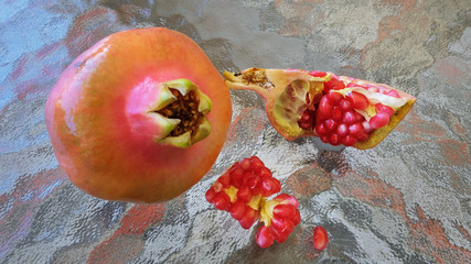 Whole pomegranate or Punica granatum fruit and few open pieces revealing white fibrous arils and thick, waxy peel, with focus on clusters of red, juicy seeds spread an abstract glass surface