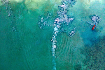 Aerial view of traditional longtail boats floating on a turquoise and clear ocean in Thailand.